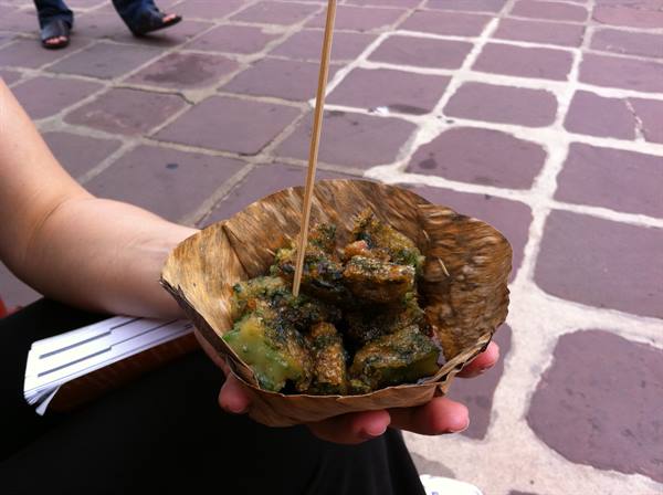 Hand holding leaf bowl with fried vegetables and skewer, on stone pavement