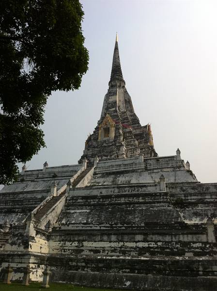 Weathered white chedi with staircase, grey sky above, dark branches at left