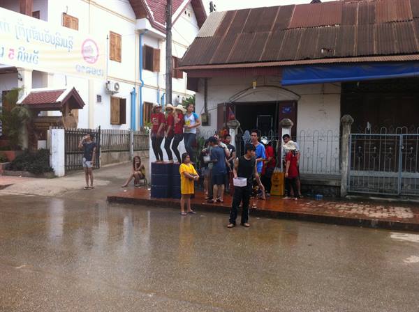Young people with buckets playfully splash water on a wet street