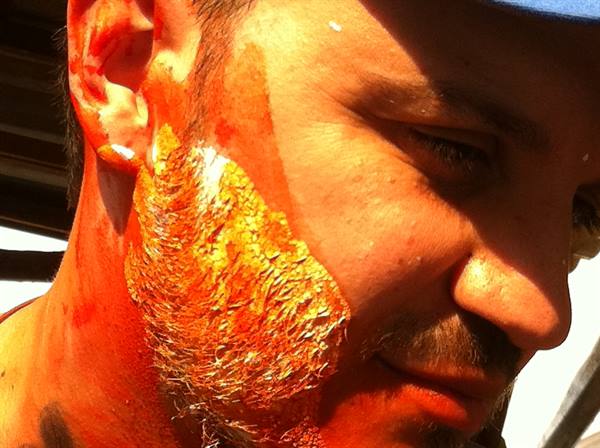 Man's face with beard covered in orange and gold paint, harsh sunlight
