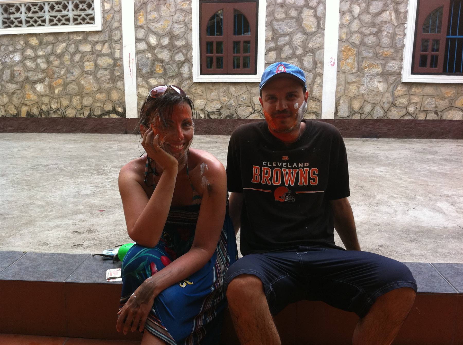 Couple with thanaka-painted faces sitting on a stone ledge by a rock wall