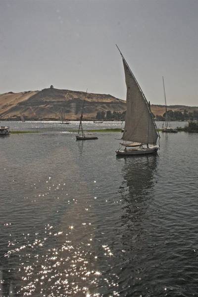 White-sailed felucca glides on sparkling Nile waters, sandy hills beyond