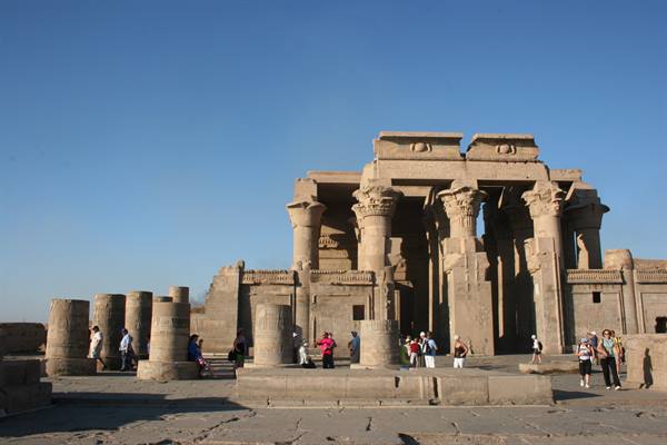Tourists among Kom Ombo temple columns, sandstone lit by morning sun