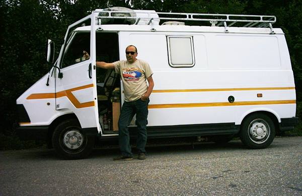 Man in sunglasses leaning on white camper van, door open