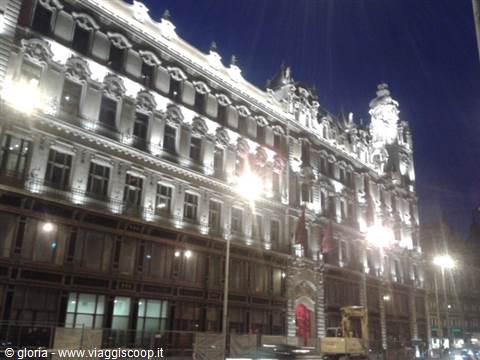 Ornate 19th-century building lit at night with red entrance, likely Paris