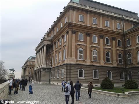Tourists walk on the cobblestones in front of Buda Castle under a grey sky