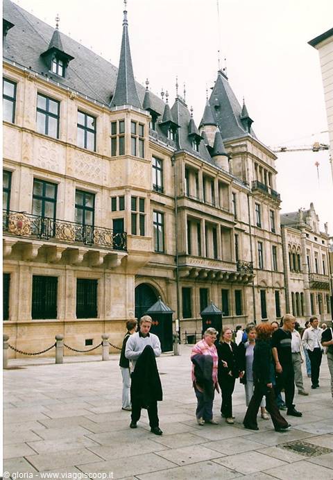 Tourists walk past the Grand Ducal Palace, light stone and pointed spires