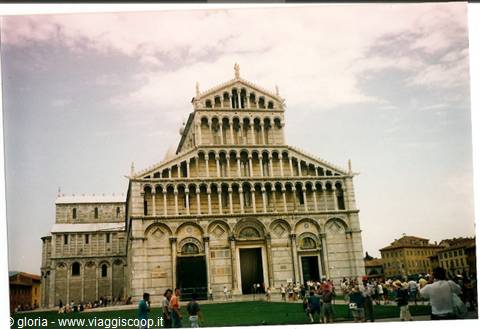 Tourists on the green lawn in front of Pisa Cathedral's Romanesque facade