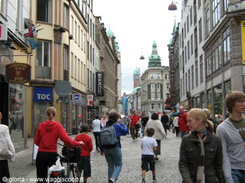 Pedestrians walking along Strøget shopping street in Copenhagen between shops and colorful facades