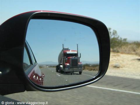 Red truck reflected in the car's side mirror on an American desert highway