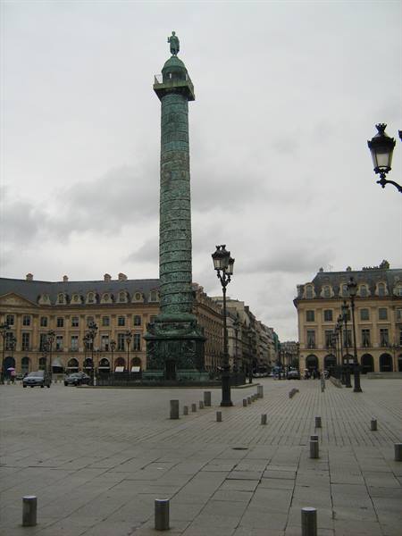 Verdigris column in Place Vendôme, Paris, among lampposts and Haussmann buildings under grey sky