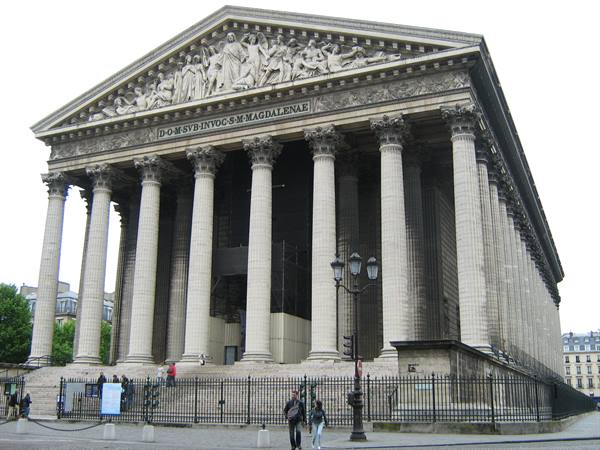 Corinthian colonnade of the Madeleine church in Paris, pedestrian walks past the fence