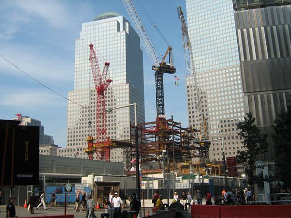 Steel cranes and construction site among glass skyscrapers, pedestrians walking at Ground Zero