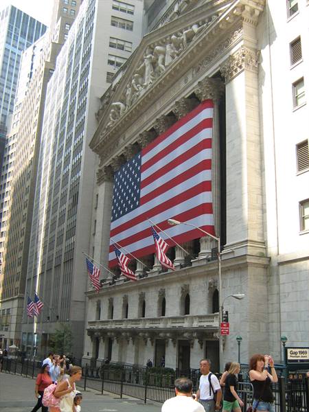 Tourists walk past the New York Stock Exchange draped with a giant American flag