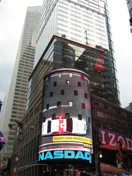 Curved NASDAQ screen with car ad in Times Square among glass towers