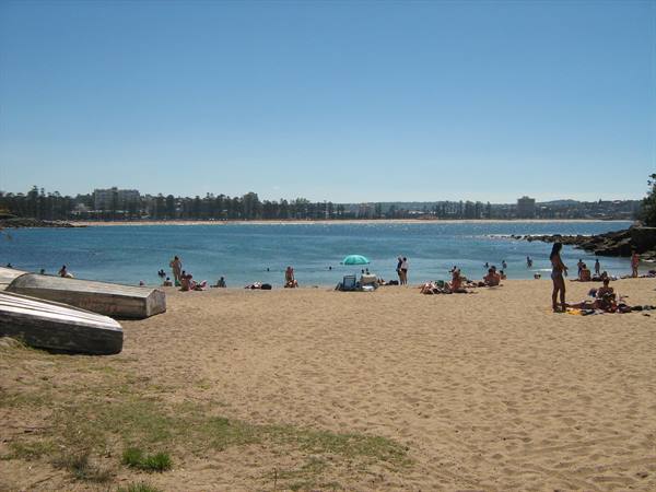 Boats on the sand and swimmers under a parasol by the turquoise sea