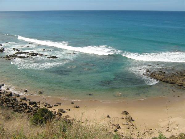 White waves on turquoise sea, dark rocks and golden sand
