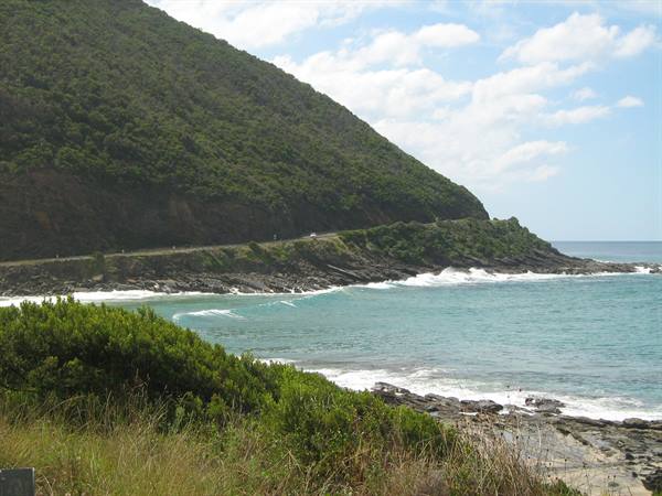 Cars on coastal road between green hillside and turquoise waves