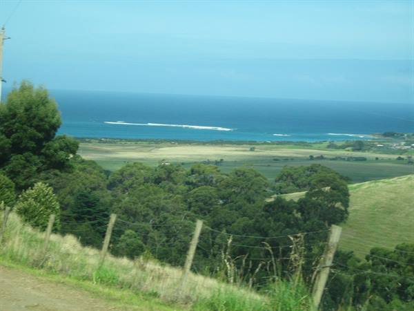 Wire fence on green hillside with trees and blue ocean waves beyond