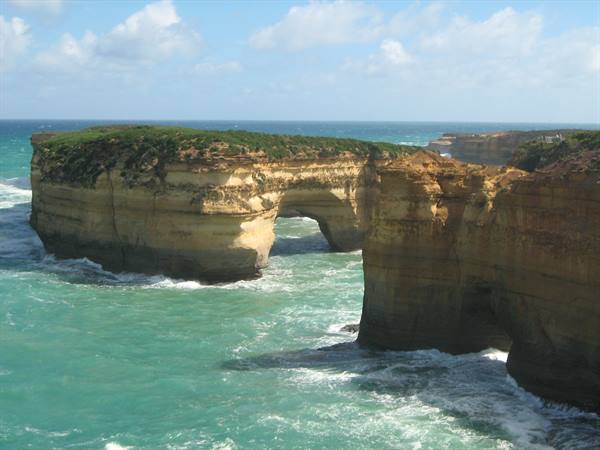 Limestone cliff with natural arch over turquoise ocean waves, London Arch