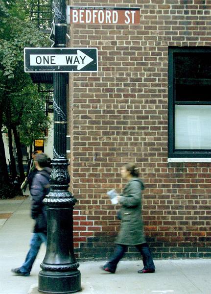 Bedford St and One Way signs on black pole, blurred pedestrians beside red bricks