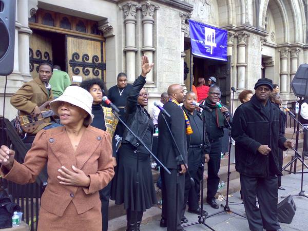 Gospel choir singing with microphones on the stone steps of a church