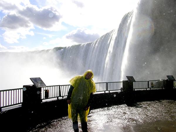Tourist in yellow poncho before Niagara Falls, spray mist and wet railing