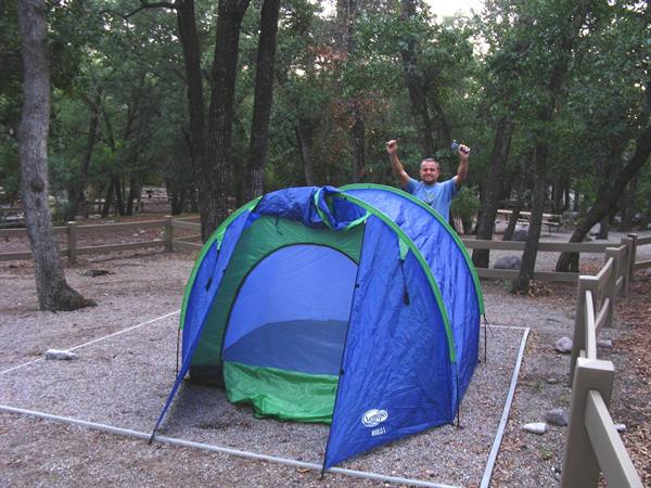 Uomo festeggia accanto alla tenda blu e verde nel campeggio di Mather, Grand Canyon
