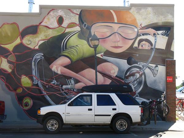 SUV bianco parcheggiato davanti a un murale di una ciclista con occhialoni