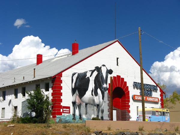 Furniture barn con mucca dipinta sul muro bianco e rosso, cielo nuvoloso