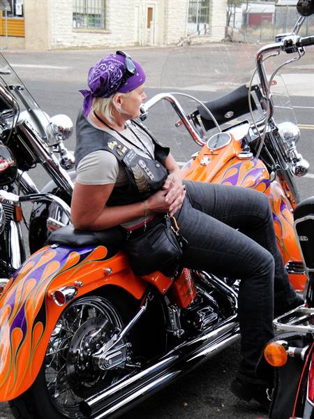 Biker con bandana viola seduta su una Harley arancio dalle fiamme
