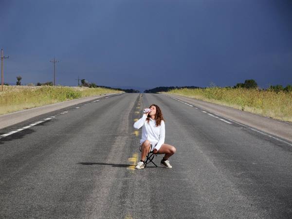 Ragazza accovacciata beve da una bottiglia in mezzo all'asfalto deserto