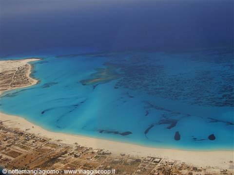 Turquoise lagoon with dark reefs, sandy beach and village seen from the plane
