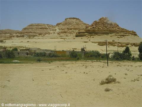 Village at the foot of sandy rock formations in Siwa, under blue sky