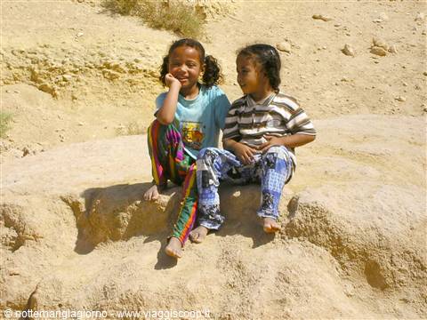 Two smiling girls sitting on sandy rock, bright sunlight