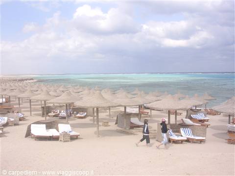Beach with straw umbrellas, empty sunbeds and two people walking by the turquoise sea