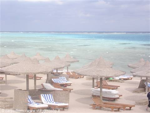 Beach with straw umbrellas and empty sun loungers facing turquoise sea