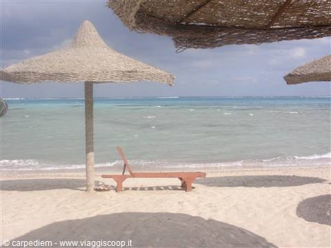 Wooden sun lounger under straw umbrellas on sandy beach, turquoise sea