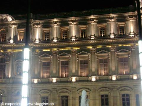 Historic palace facade lit at night, pedimented windows and glowing lamppost