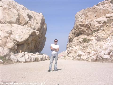 Man in white t-shirt standing between two huge limestone rocks under blue sky