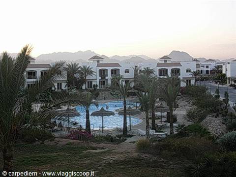 Pool amid palms and straw umbrellas, white resort buildings and mountains at dawn