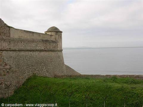 Stone fortress walls with a sentry turret overlooking the calm sea under cloudy sky