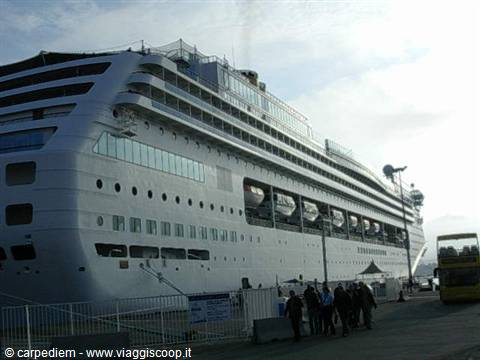 White cruise ship docked at port, passengers walking along the pier
