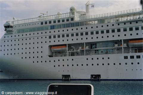 White cruise ship docked at port, orange lifeboats and rows of windows