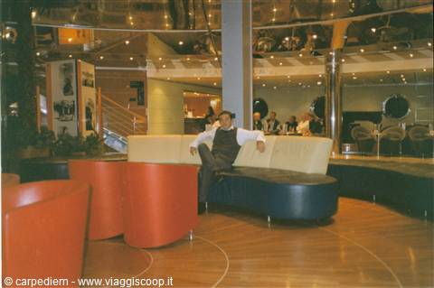 Man sitting on curved sofa in a lounge with red armchairs and lights