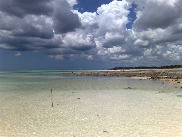 Clear water over white sand, towering clouds and rocky shoreline