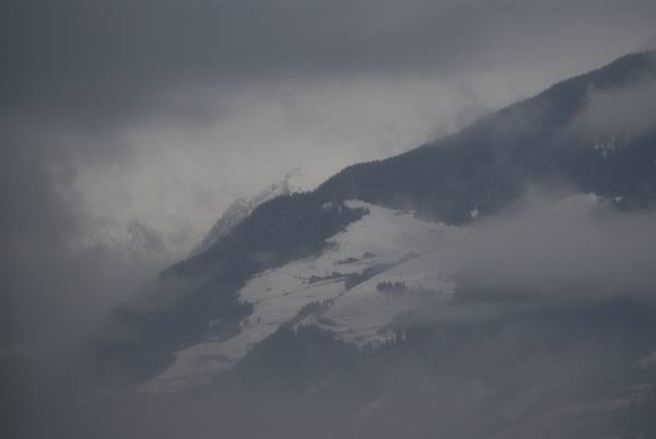 snowy mountains wrapped in fog, dark forests under grey sky