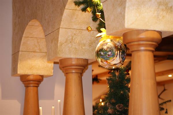 Wooden columns under stone arches, golden Christmas bauble and decorated tree