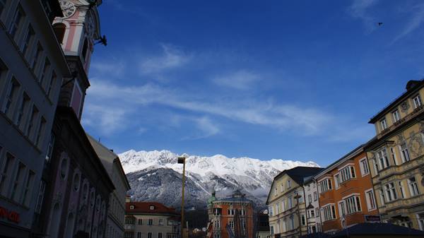 Colourful historic buildings and snowy mountain chain under blue sky in Innsbruck
