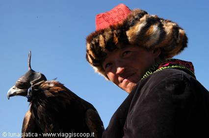 Hunter in fur hat with red top holding a golden eagle